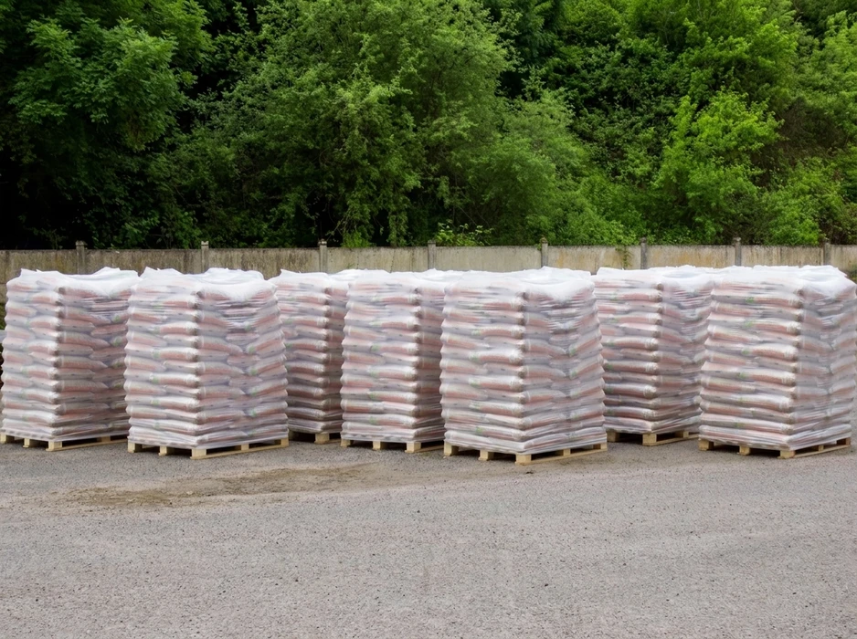 Cinq palettes en bois alignées en extérieur, chargées de sacs de granulés de bois (pellets), conditionnés en big bags individuels sous film plastique étirable transparent