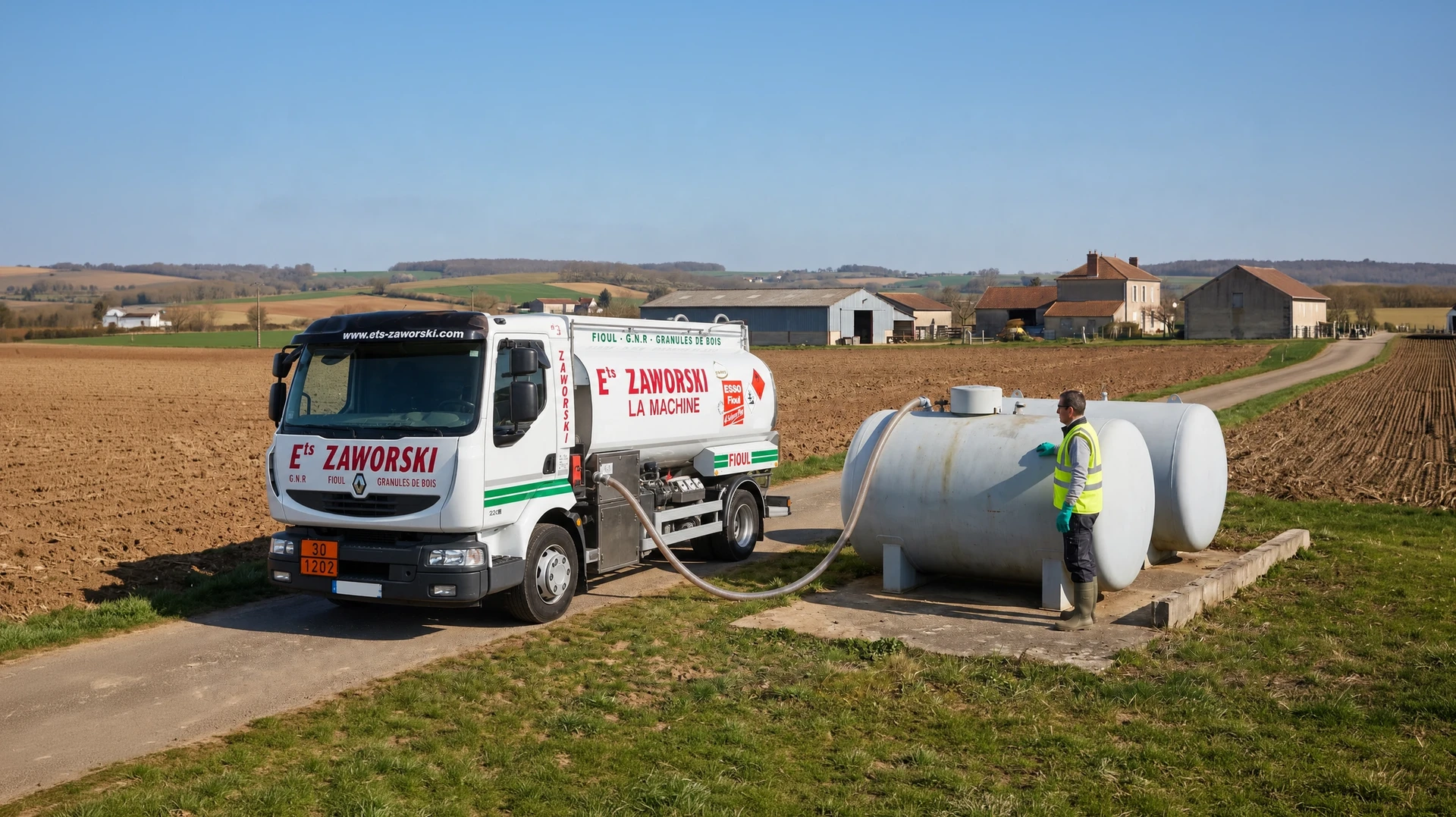 Camion-citerne blanc aux couleurs d'Ets Zaworski stationné en bordure de champ agricole, tuyau de remplissage déployé vers une cuve de stockage cylindrique posée au sol, distributeur en train de livrer du GNR supérieur Esso à une exploitation agricole. Ciel dégagé, végétation rurale environnante.