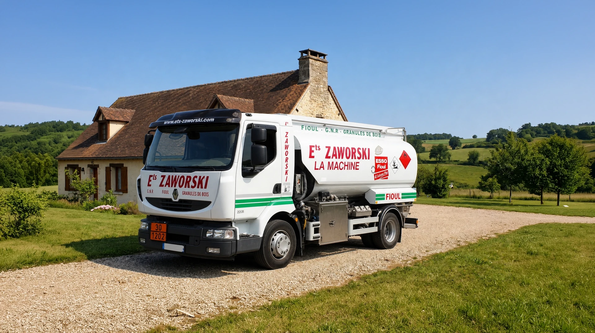 Camion-citerne blanc Iveco Eurocargo stationné en extérieur devant une maison équipée d'une cheminée. Véhicule de profil montrant la cuve cylindrique inox, les marquages ADR oranges (30/1202), le logo Ets Zaworski visible sur la carrosserie, la rampe de distribution latérale avec compteur et tuyauterie de livraison, le tout en contexte de livraison résidentielle dans un environnement rural avec végétation.